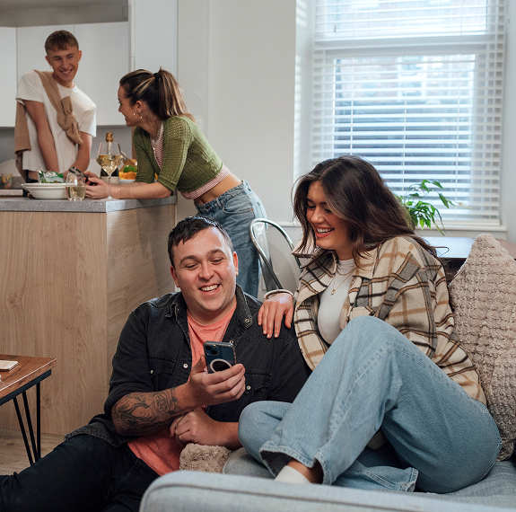 Friends sitting together in a kitchen, referring each other to Utilita Energy using the My Utilita App.
