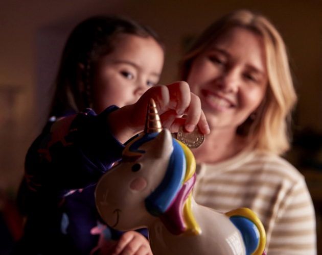 A mother and daughter in their energy-efficient home, saving money in a piggy bank by using
                   Utilita’s Power Price List